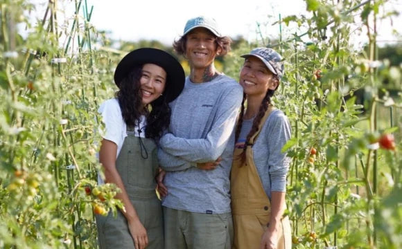 畑で笑顔を見せる3人の不耕起栽培農家のポートレート。背景には緑豊かなトマトの植物が見える。