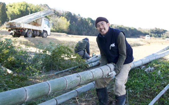 畑で竹の柵を設置する作業を行っている農家の人々。前景にはカメラに向かって笑顔を見せる男性がいる。